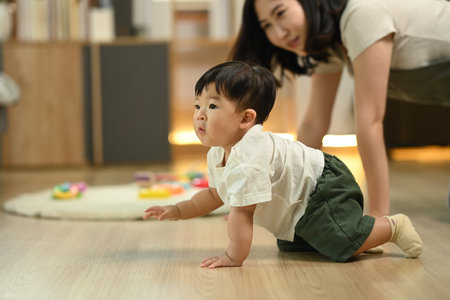 Adorable little baby boy learning to crawl with supportive mother closely watching. Child development concept.の写真素材