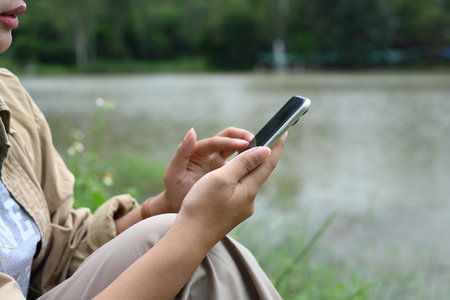 Young woman using mobile phone near lake. People, lifestyle and technology concept.の写真素材