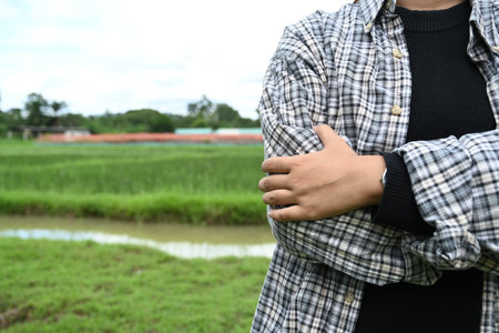 Confident farmer wearing a plaid shirt standing with arms in a lush rice field.の写真素材