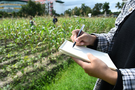 Cropped shot of farmer taking notes on a notepad while inspecting cornfield.の写真素材