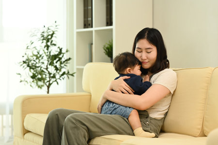Loving young mother cuddling her baby boy sitting on sofa. Parenting, childcare and family concept.の写真素材