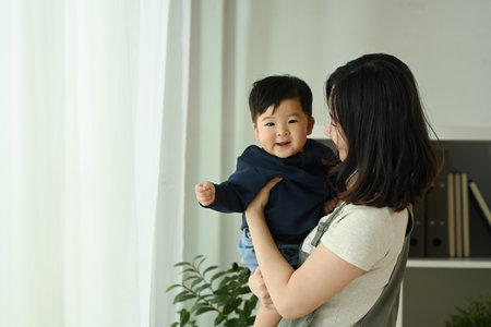 Loving asian mother holding her smiling baby in her arms. Family, love and childcare concept.の写真素材