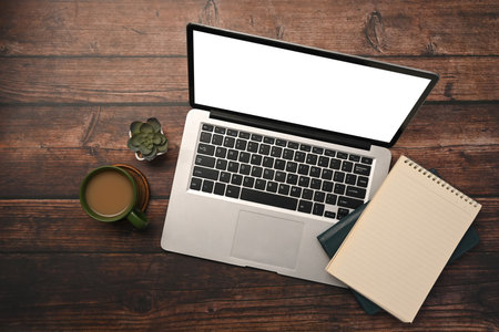 Above view laptop with white screen, notepad and coffee cup on wooden table.