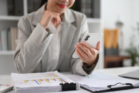 Cropped shot smiling businesswoman using mobile phone at working desk.の写真素材