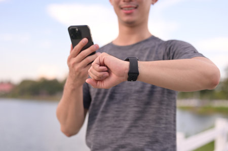 Athletic man holding mobile phone and checking heart rate on smartwatch.