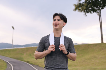 Smiling young asian man jogging in the park on cloudy day. Fitness and active lifestyle.