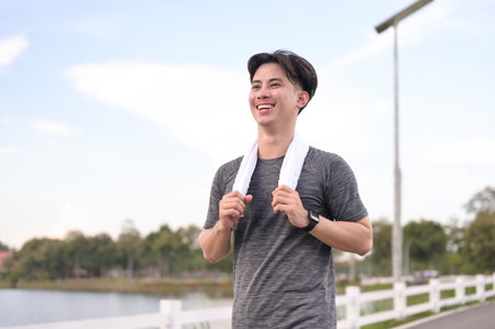 Smiling young asian man jogging in the park on cloudy day. Fitness and active lifestyle.の写真素材