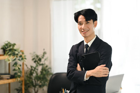 Portrait of young businessman in a suit holding a digital tablet standing in office.の写真素材