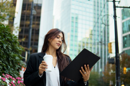 Businesswoman reviewing work documents during coffee break in modern cityscape.の写真素材