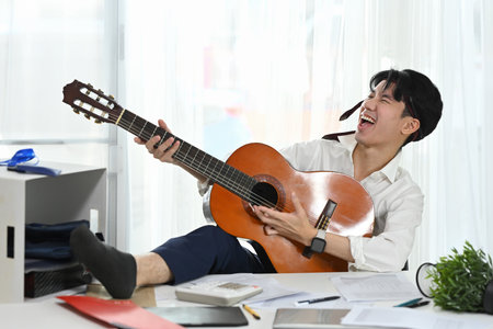 Cheerful male employee with necktie around his head enjoying a music break amidst busy workday.の写真素材