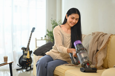 Young woman using handheld vacuum to clean living room furniture.の写真素材