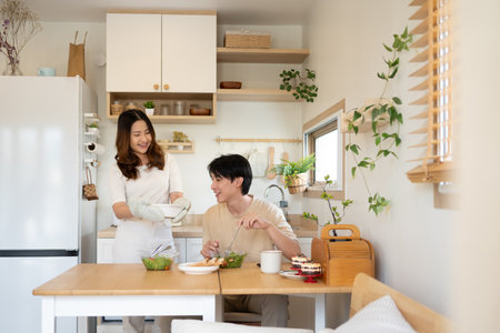 Young asian woman serving healthy lunch to her husband in a minimalist kitchen.の写真素材