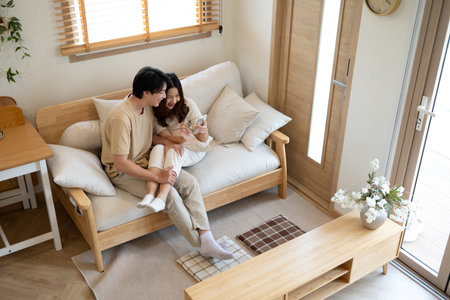 Loving asian couple sharing a cozy moment while browsing on smartphone at home.の写真素材