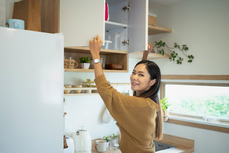Smiling young woman organizing kitchen cabinet in cozy home.の写真素材