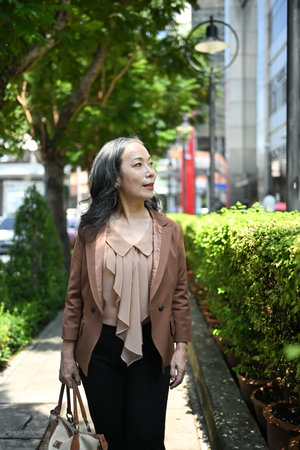 Positive mature businesswoman strolling through an urban park on beautiful day.の写真素材