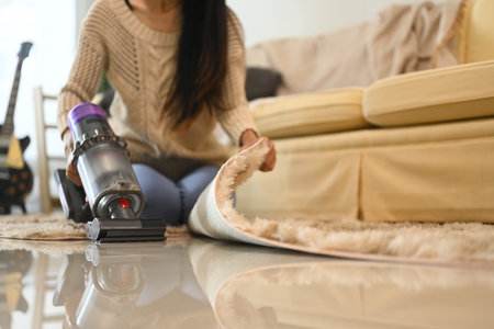 Young woman doing housework, vacuuming floor with a cordless vacuum cleaner.の写真素材