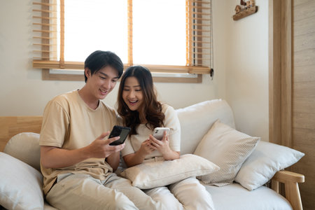 Relaxed asian couple watching online content on a smart phone in the living room.の写真素材
