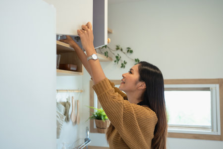 Beautiful woman reaching for ingredients in upper kitchen cabinets.の写真素材