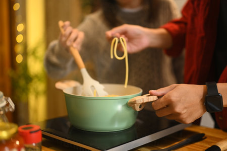 Close up of couple cooking pasta together in a warm kitchen during the festive season.の写真素材