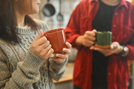 Relaxed young couple enjoying warm drinks together in kitchen.