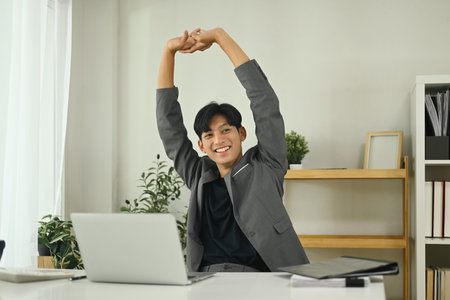 Relaxed office worker stretching after work session in the workplace.の写真素材