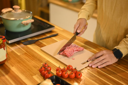 Young man chopping meat on kitchen counter with fresh ingredients.