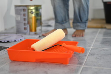 Close up image of a paint roller resting in bright orange tray, ready for use in painting project.の写真素材
