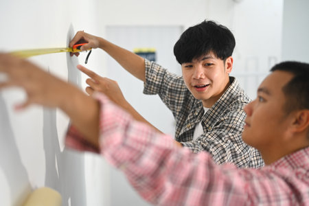 Two young men measuring a wall preparing for a home improvement project.の写真素材