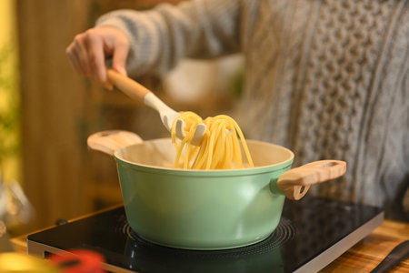 Close up of woman preparing spaghetti in a cozy kitchen.の写真素材