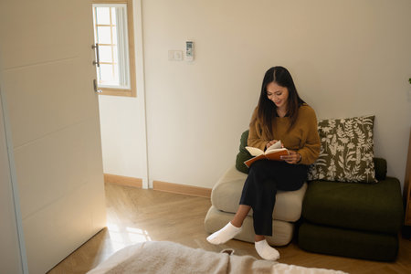 Peaceful young woman relaxing and reading in a modern living space.の写真素材