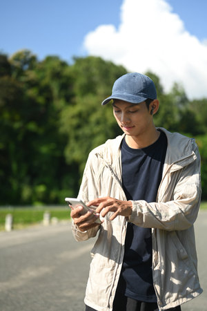 Young sportsman runner with earphones using mobile phone in the park.の写真素材