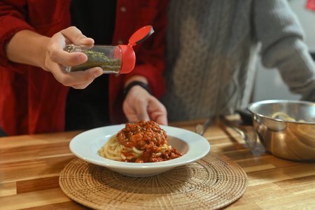 Close up of man sprinkling dried herbs from a spice jar over a plate of spaghetti.の写真素材