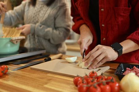 Close up of man chopping onions on a cutting board surrounded by fresh ingredients.