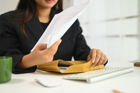 Businesswoman in a formal suit working at a desk, organizing documents from a brown envelope.の写真素材
