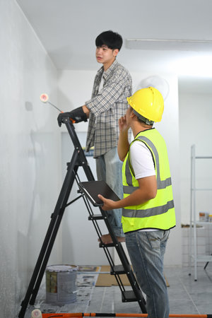 Asian male worker applying paint under the guidance of project manager.の写真素材