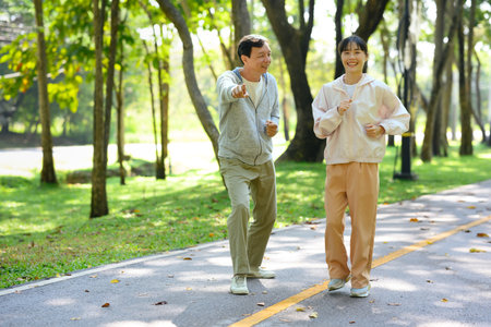 Cheerful young asian woman jogging with her father in park. Family activities, health and wellbeing concept.の写真素材