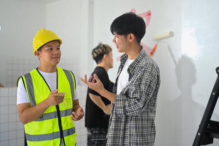 Shot of supervisor in hardhat discussing plans with painter standing inside house.の写真素材