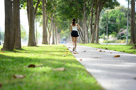 Back view of young slim sportswoman jogging in the park on beautiful day.の写真素材