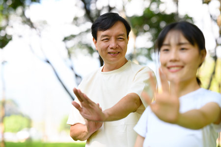 Smiling middle aged father and daughter practicing Tai Chi in a peaceful garden.の写真素材