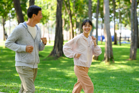 Cheerful asian woman and her father jogging through a scenic park in the morning.の写真素材