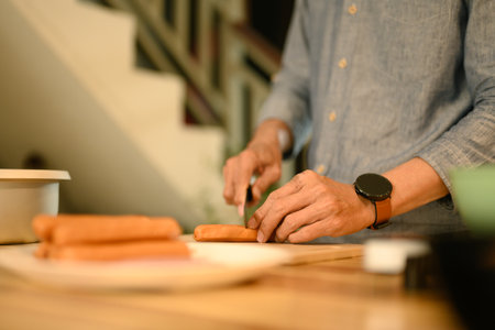 Close up of senior man slicing sausages with a knife on a wooden countertop.の写真素材