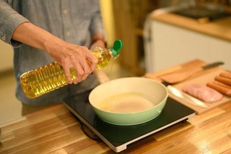 Cropped shot man pouring oil into a frying pan during meal preparation.の写真素材