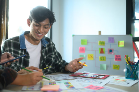 Cheerful young man collaborating with his team on app design and UI UX development in the office.