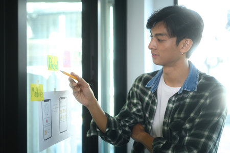 Young designer analyzing design elements and sketching to visualize ideas on a glass board.