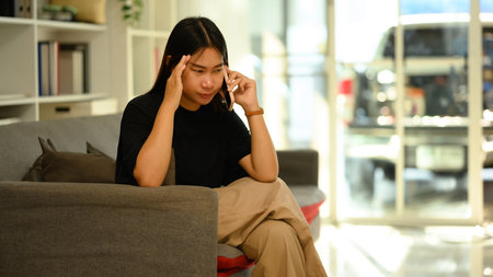 Frustrated young woman talking mobile phone while sitting on the sofa.の写真素材