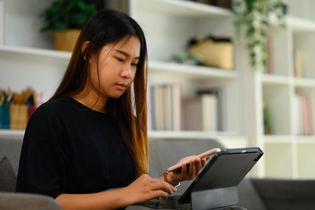 Focused young woman holding her smartphone working attentively on digital tablet.の写真素材