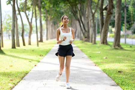 Smiling African athletic woman jogging along a pathway in a sunny park.の写真素材
