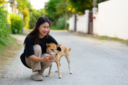 Cheerful young woman kneeling down next to dog and taking a picture with her mobile phone.の写真素材