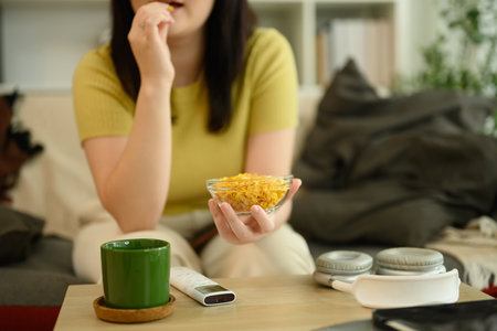 Young woman holding a bowl of cornflakes sitting in a cozy living room.の写真素材