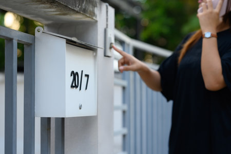 Minimalistic white mailbox on a gate with young woman ringing a doorbell on background.の写真素材